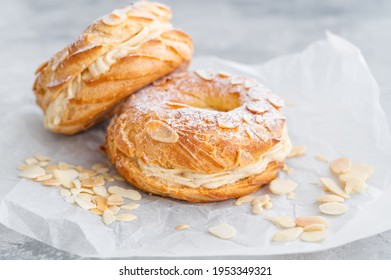 French Traditional Cake Paris Brest With Praline Cream, Powdered Sugar And Almond Petals On Top On A Gray Concrete Background. Copy Space