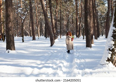 Fresh air. Positive red haired woman in warm clothes looking around while walking through rural winter forest and holding yellow snowdrops in hands