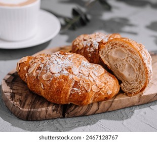 Fresh almond croissants on a wooden board with latte art coffee in the background - Powered by Shutterstock