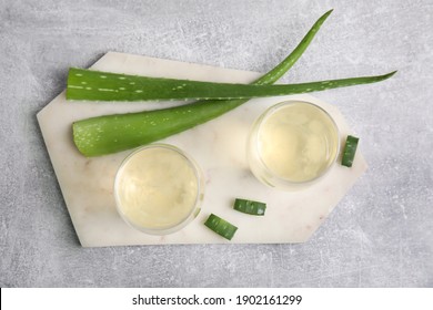 Fresh aloe drink in glasses and leaves on light grey table, flat lay