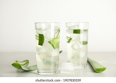 Fresh aloe drink in glasses and leaves on light table