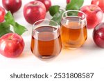 Fresh apple juice in glasses, fruits and green leaves on white table, closeup