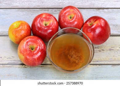 Fresh apples and a bowl of raw and unfiltered organic apple cider vinegar with mother enzymes