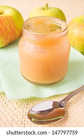 Fresh applesauce (apple puree, babyfood) in glass jar with green apples and spoon close up, horizontal, vegetarian