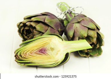 Fresh artichokes bundle tied with a ribbon on a white wooden table