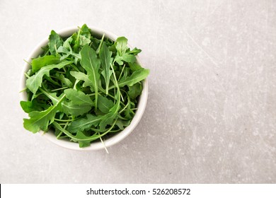 Fresh Arugula Salad On A Grey Stone Background.