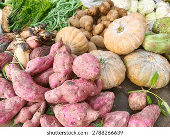 Fresh assorted root vegetables and squashes displayed in a market pile, including beets, potatoes, onions, and gourds.
