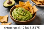 
Fresh avocado guacamole dip, vibrant and creamy, served with salted tortilla chips in a wooden bowl. A perfect snack on a grey marble table.