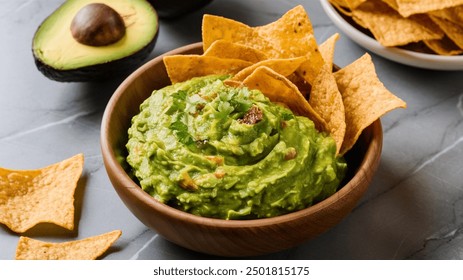 
Fresh avocado guacamole dip, vibrant and creamy, served with salted tortilla chips in a wooden bowl. A perfect snack on a grey marble table. - Powered by Shutterstock