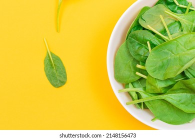 Fresh Baby Spinach Leaves in White Bowl on Yellow Background - Top View. Vegan and Vegetarian Culture. Raw Food, Green Leaves. Healthy Diet