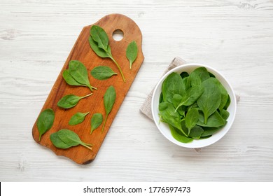 Fresh Baby Spinach In A White Bowl On A White Wooden Table, Top View. Overhead, From Above, Flat Lay. 