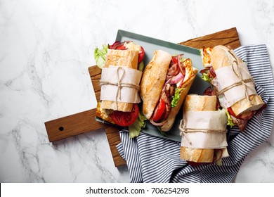 Fresh baguette sandwich bahn-mi styled. Bacon, roasted cheese, tomatoes and lettuce on metallic tray on white marble background.