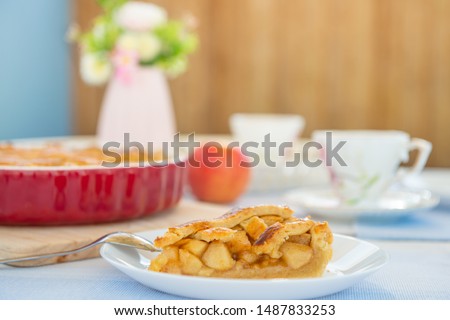Fresh baked apple pie, cup of tea and flowers on a table at home on cozy terrace