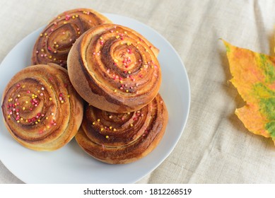 Fresh Baked Cinnamon Rolls Or Buns With Sugar Sprinkle Topping On White Plate And Autumn Leaf On Table, Top View, Lifestyle Stock Photo Image Background With Copy Space