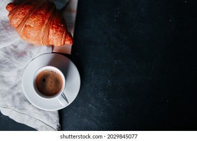 Fresh baked croissant on linen napkin, mug of expresso on dark concrete table. Cup of hot coffee, buns, rolls close up. Food, French breakfast, morning menu, cafe concept. Top view, copy space