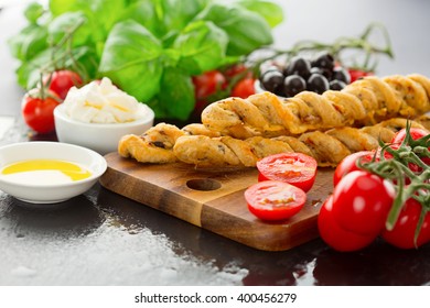 Fresh baked homemade grissini bread sticks with olive oil, tomatoes cherry and basil leaves over dark background, selective focus