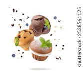 Fresh baked muffins with chocolate chips, blueberry berries, vanilla, sugar powder, crumbs and mint leaves flying isolated on white background. Muffin or cupcake closeup as dessert for coffee break. 