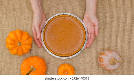 Fresh Baked Pumpkin Pie In Disposable Baking Pan Close Up In Woman Hands On Rustic Background, Flat Lay