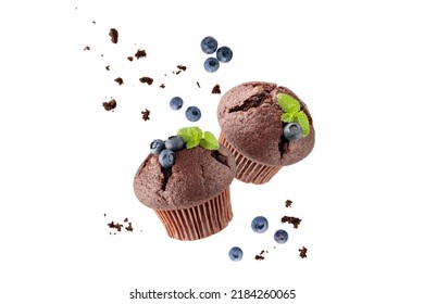 Fresh baked two chocolate muffins with blueberry berries, crumbs and mint leaves flying on white background. Sweet cupcake falling. Pastry card with copy space