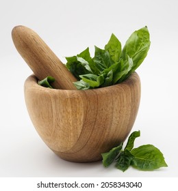 Fresh basil leaves in a wooden mortar. Isolated on white background.