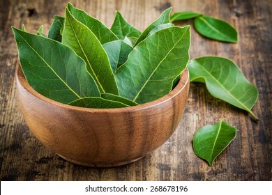 Fresh bay leaves in a wooden bowl on a rustic wooden background