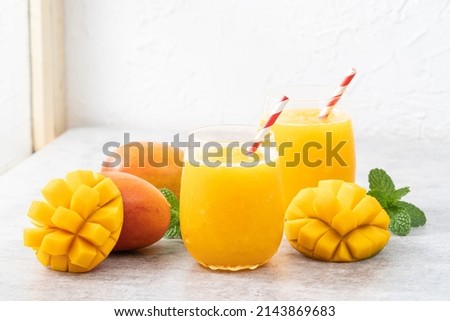 Fresh beautiful delicious mango juice. Close up design concept of smoothie cold drink in a glass cup with paper straw on gray table background.