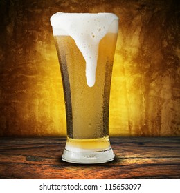 Fresh Beer In Glass With Foam Spills On Yellow Background