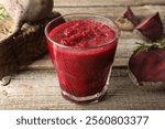 Fresh beetroot smoothie in glass, rosemary and cut vegetables on wooden table, closeup