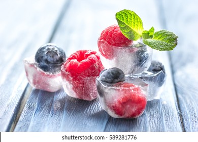fresh berries with mint in ice cubes on wooden background