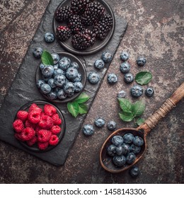 Fresh berries with raspberries, blueberries, blackberries in bowl on a stone stand on a dark metal background.