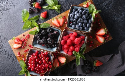 Fresh berries. Red currants, blackberries, blueberries and raspberries in bowls on a large wooden board with mint leaves, strawberries and pomegranate seeds. Background image, top view, horizontal - Powered by Shutterstock