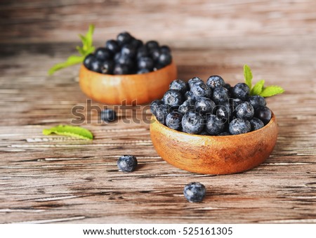 fresh bilberries or blueberries in small wooden bowls on a rustic table, selective focus