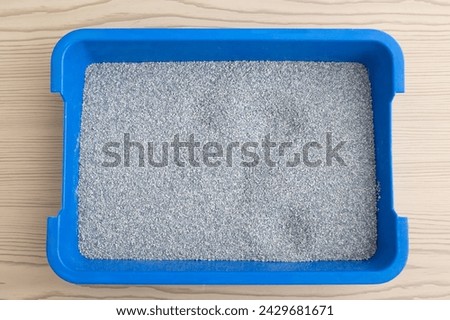  Fresh blue cat litter box filled with fine grey litter on a wooden floor. Cat hygiene and health concept. 