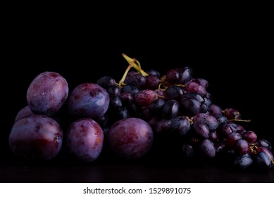 fresh blue plums and grapes on a black reflective background