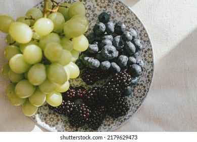 Fresh Blueberries, Blackberries And Grapes In Sunlight On Ceramic Plate Flat Lay. Healthy Food Aesthetics. Summer Berries In Light On Soft Linen Background. Moody Banner