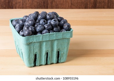 Fresh Blueberries In Green Pint Container On Wooden Table