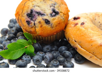 Fresh Blueberries Surround A Single Blueberry Muffin And A Bagel On A Light Background