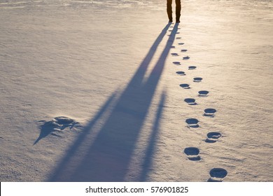 Fresh boots footprints with human shadow in the snow in the sunset light in winter evening. Background.
