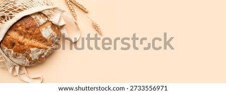 Fresh bread in mesh cotton string bag, ears of wheat on beige background, flat lay top view. Eco-friendly shopping, zero waste. Crispy loaf of artisan bread from the bakery