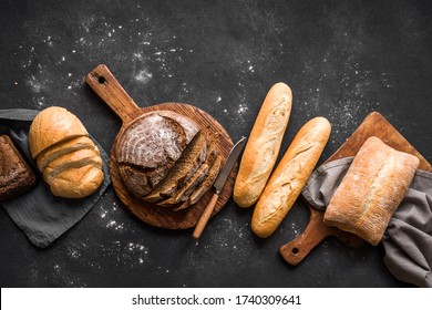 Fresh Bread on black background, top view, copy space. Homemade fresh baked various loafs of wheat and rye bread flat lay.