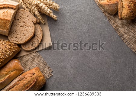 Fresh bread on stone table, copy space, top view. Brown and white whole grain loaves still life composition with wheat ears scattered around.