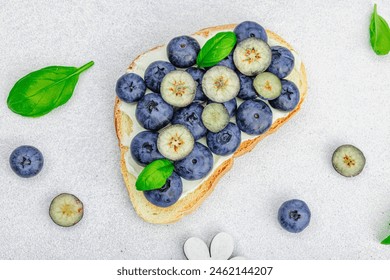 Fresh bread sandwiches with sweet blueberries, cream cheese and basil leaves. Good morning breakfast concept. White stone concrete background, flat lay, top view - Powered by Shutterstock