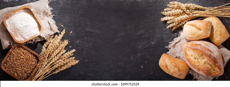 fresh bread with wheat ears and bowl of flour on dark board, top view - Shutterstock ID 1099752539