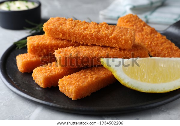 Fresh breaded fish fingers and lemon served on\
light grey table, closeup