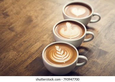 Fresh Brewed Coffees With Beautiful Latte Art On Surface, Three Cup In A Row On Wooden Table Ready To Drink