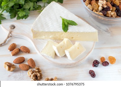 Fresh Brie Cheese And A Slice On A Wooden Board With Nuts