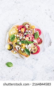 Fresh bright tomato salad from colorful tomatoes with feta cheese, basil and olive oil. Vegetarian and vegan food. Concept for a tasty and healthy meal. Top view. Copy space.