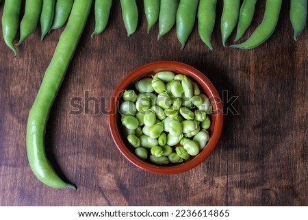 Fresh broad beans next to a clay plate with its fruit