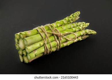 Fresh bunch of green asparagus tied with jute cord over a black background. Spring vegetable, eco friendly packaging