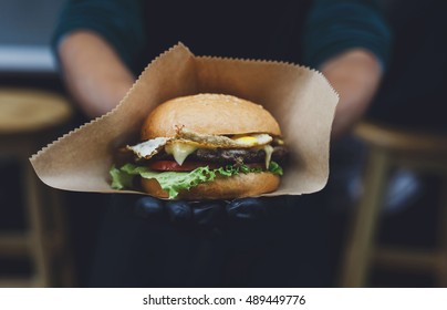 Fresh burger cooked at barbecue outdoors in craft paper. Cookout american bbq food. Big hamburger with steak meat and vegetables closeup with chef unfocused at background. Street food, fast food. - Powered by Shutterstock